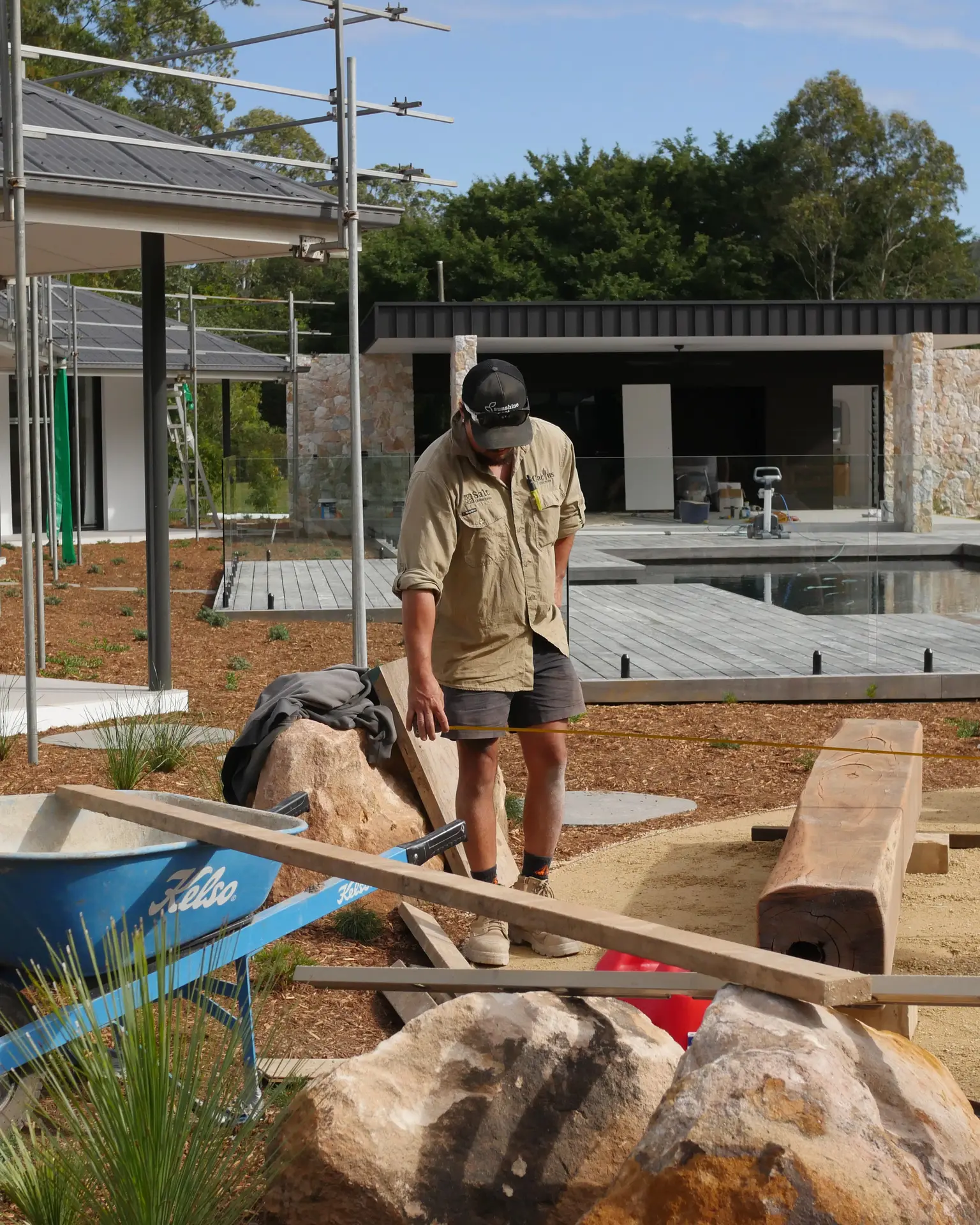 Salt Landscaping crew member setting out timber sleepers and boulders beside a new pool deck on a residential landscape construction site