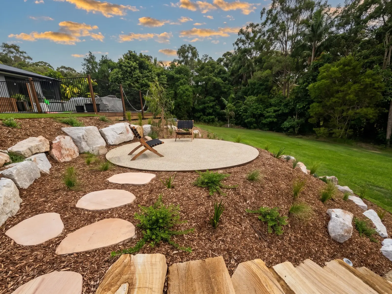 A finished Salt Landscaping garden with a gravel seating circle and sandstone steppers at dusk